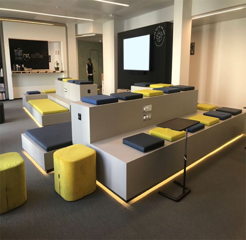 Gradins en bois avec assises jaunes et bleues face aux écrans d'un espace multimédia